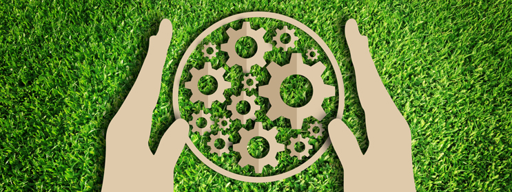 paper cut-out of gears in a circle held by two hands on a green grassy background denoting environmentally friendly practices