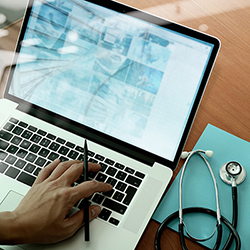 photo of doctor using laptop with stethoscope nearby