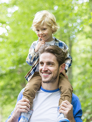 photo of man walking in woods with his son on his shoulders